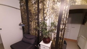 Ein kleiner, moderner Raum mit einem dunklen Sofa, einer kleinen weißen Kommode, einer Lampe und einer Wand mit vertikalem Garten.