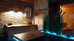 Ein Badezimmer mit Steinwand, Holzboden, einem Waschbecken und einer blau beleuchteten Wassereinrichtung.