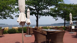 Outdoor seating with tables and chairs, a view of the sea, and a lighthouse in the distance. - Penthouse vacation apartment "Auszeit" 100 m from the center. Beach, preferably with dog, WLan incl. (Laboe)