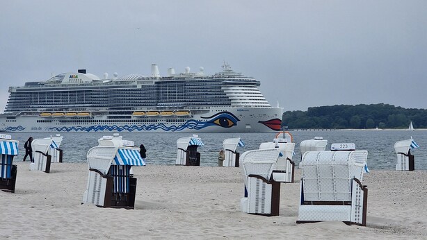 A cruise ship docked at a beach with beach chairs and umbrellas. - Penthouse vacation apartment "Auszeit" 100 m from the center. Beach, preferably with dog, WLan incl. (Laboe)