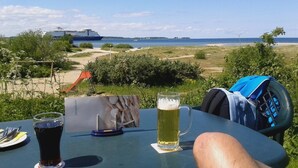 A table with a drink, a menu, and a view of the sea and a ship. - Penthouse vacation apartment "Auszeit" 100 m from the center. Beach, preferably with dog, WLan incl. (Laboe)
