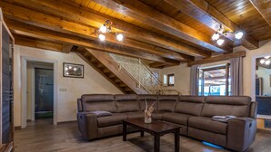 Ein geräumiges Wohnzimmer mit einem großen, winkelförmigen Sofasessel, einem Holztisch und einer Treppe mit aufwendiger Geländerarbeit.