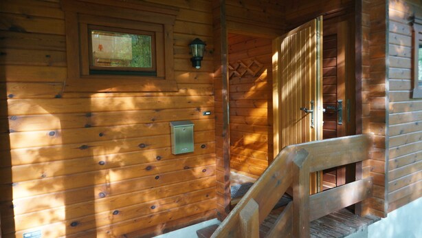 L’intérieur d’une cabane en bois, avec un escalier en bois, un luminaire fixé au mur et une petite fenêtre.