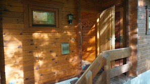 Interior de uma cabana de madeira com escada de madeira, luminária na parede e uma pequena janela.