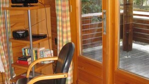 Un intérieur en bois, avec un fauteuil en cuir noir, un téléviseur posé sur une étagère et une grande porte-fenêtre coulissante donnant sur un espace extérieur.