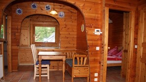 Une cabane en bois comprenant un coin repas, un lit et une fenêtre donnant sur un paysage verdoyant.