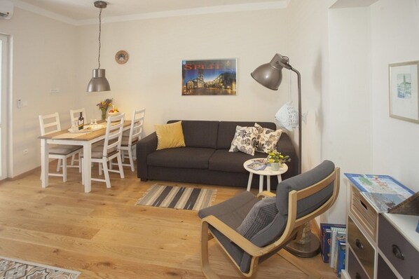 A living room with a dark sofa, a wooden dining table with chairs, a side table with a lamp, and a bookshelf. - ****Apartment Xenios with sea view, promenade, old town, balcony (Split)