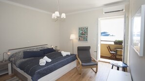 Ein Schlafzimmer mit Bett, Stuhl, Schreibtisch, Lampe und Blick ins Freie.