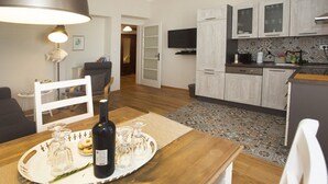 Eine moderne Küche mit weißen Schränken, einem Essbereich mit Holztisch und einem Fernseher, der über den Schränken angebracht ist.