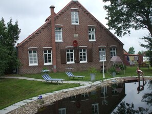 A brick house with a large window, a small garden, and a pond. - Spacious exclusive apartment on the 1st floor with a natural pond (Wittmund-Buttforde)