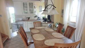 Un comedor con una mesa y sillas de madera, una cocina al fondo y una ventana con cortinas.