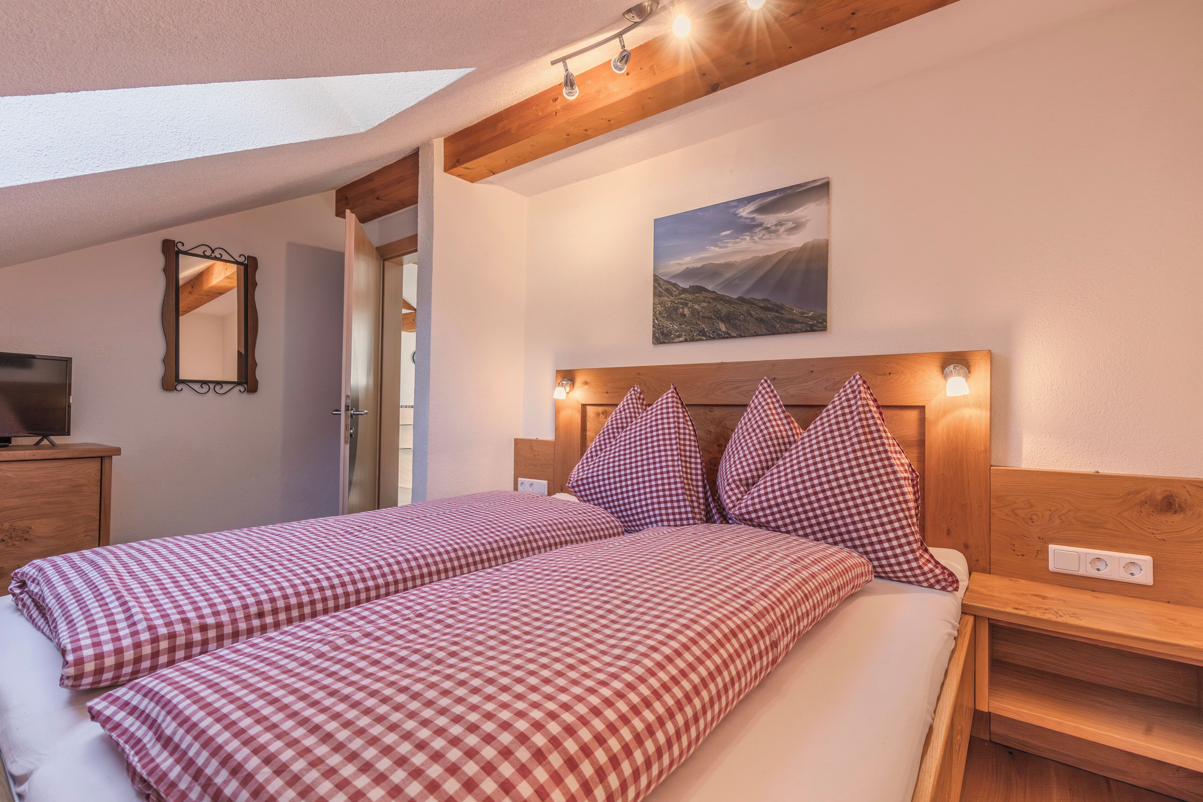 A bedroom with two beds, wooden headboards, a painting, and a mirror.