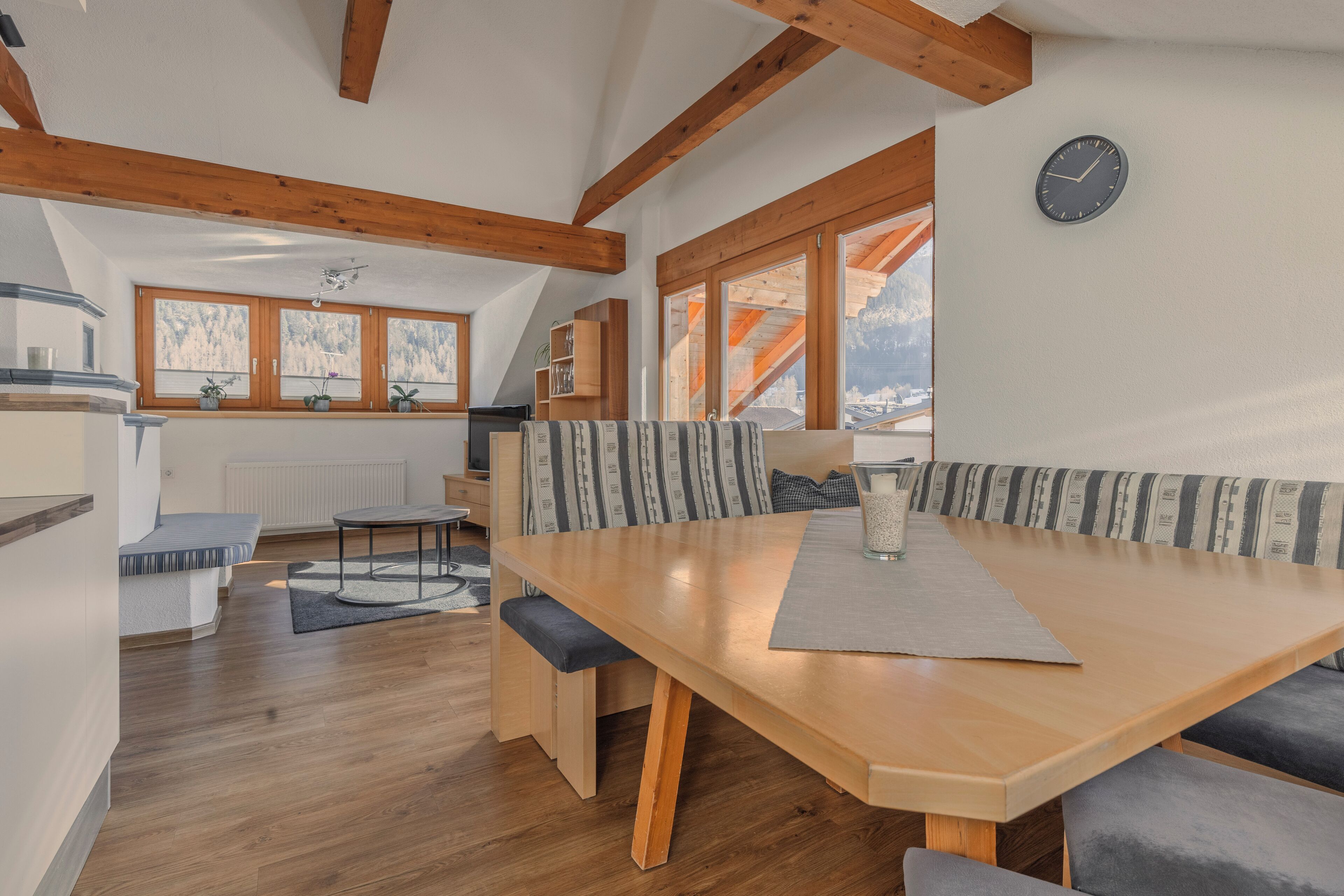 Un coin repas accueillant avec une table en bois, des bancs et une vue sur les montagnes grâce à de grandes fenêtres.