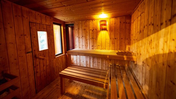 Un sauna en bois, doté de bancs et d’un luminaire fixé au mur.
