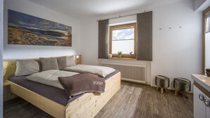A bedroom with a wooden bed, a window with a view, a radiator, and a small stool.