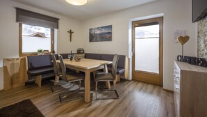 A modern dining area with a wooden table and chairs, a bench, and a view of mountains through the windows.