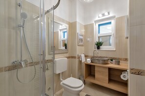 A modern bathroom with a glass-enclosed shower, a wooden vanity with a large sink, and a toilet.