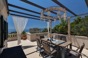 An outdoor patio with a table set for dining, a pergola with decorative elements, and a view of the sea.