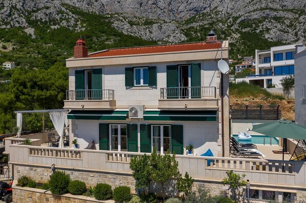 A two-story building with a balcony, a satellite dish, and a pool area with lounge chairs and a swan float.