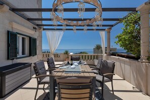 An outdoor patio with a table set for dining, surrounded by chairs, and a pergola with hanging chandeliers.