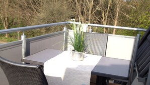 A deck with a table and chairs, a potted plant, and a railing.
