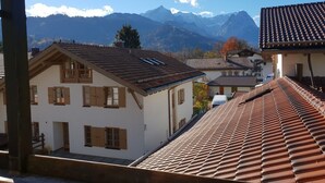 Een traditionele chalet met een schuin dak, houten luiken en uitzicht op bergen.