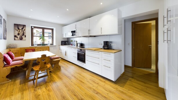 Een moderne keuken met witte kasten, een houten aanrecht en een eethoek met een houten tafel en stoelen.