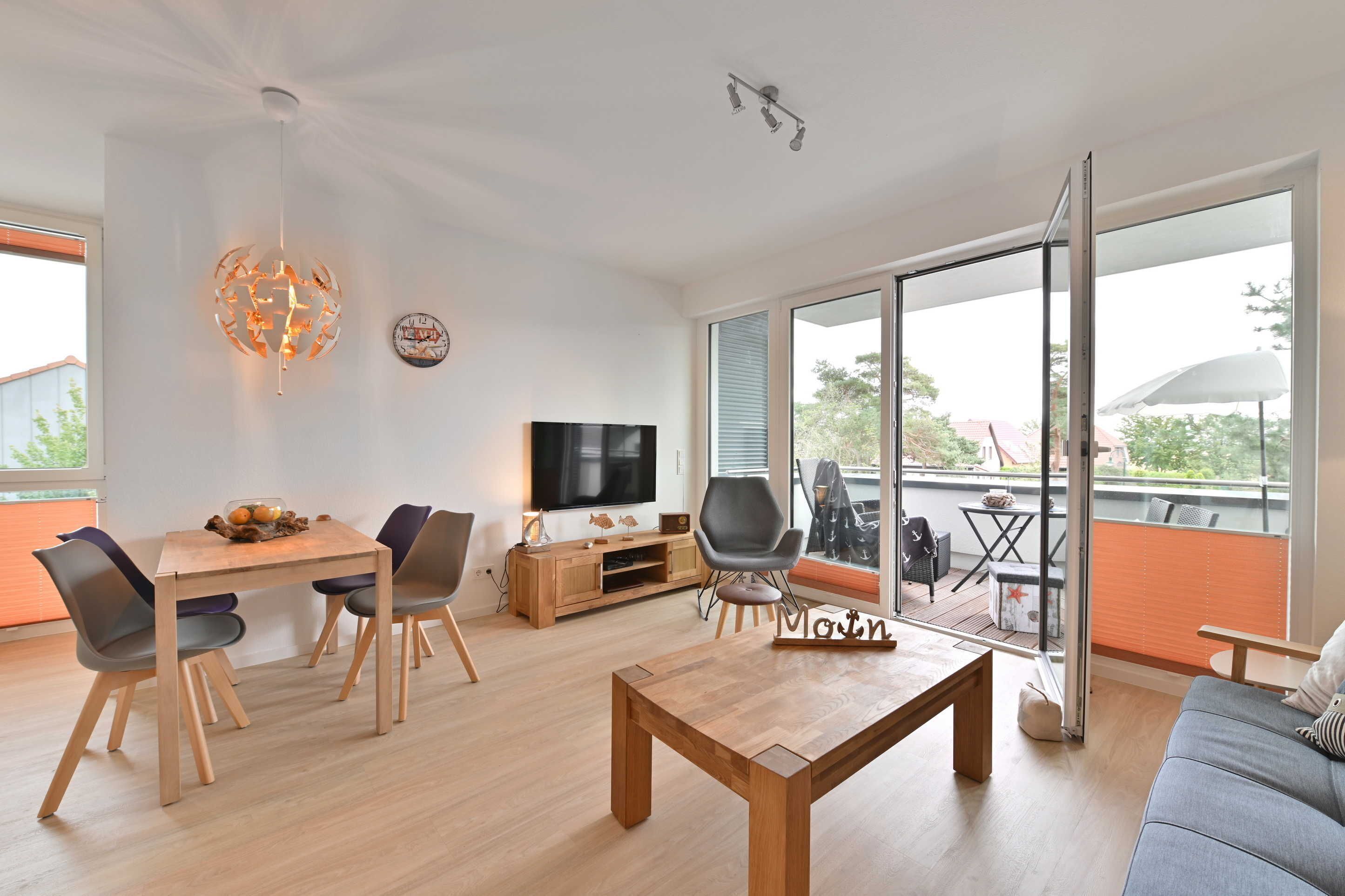Een moderne woonkamer met een houten salontafel, een bank, een eethoek met stoelen, een televisie en een balkon met tuinmeubilair.