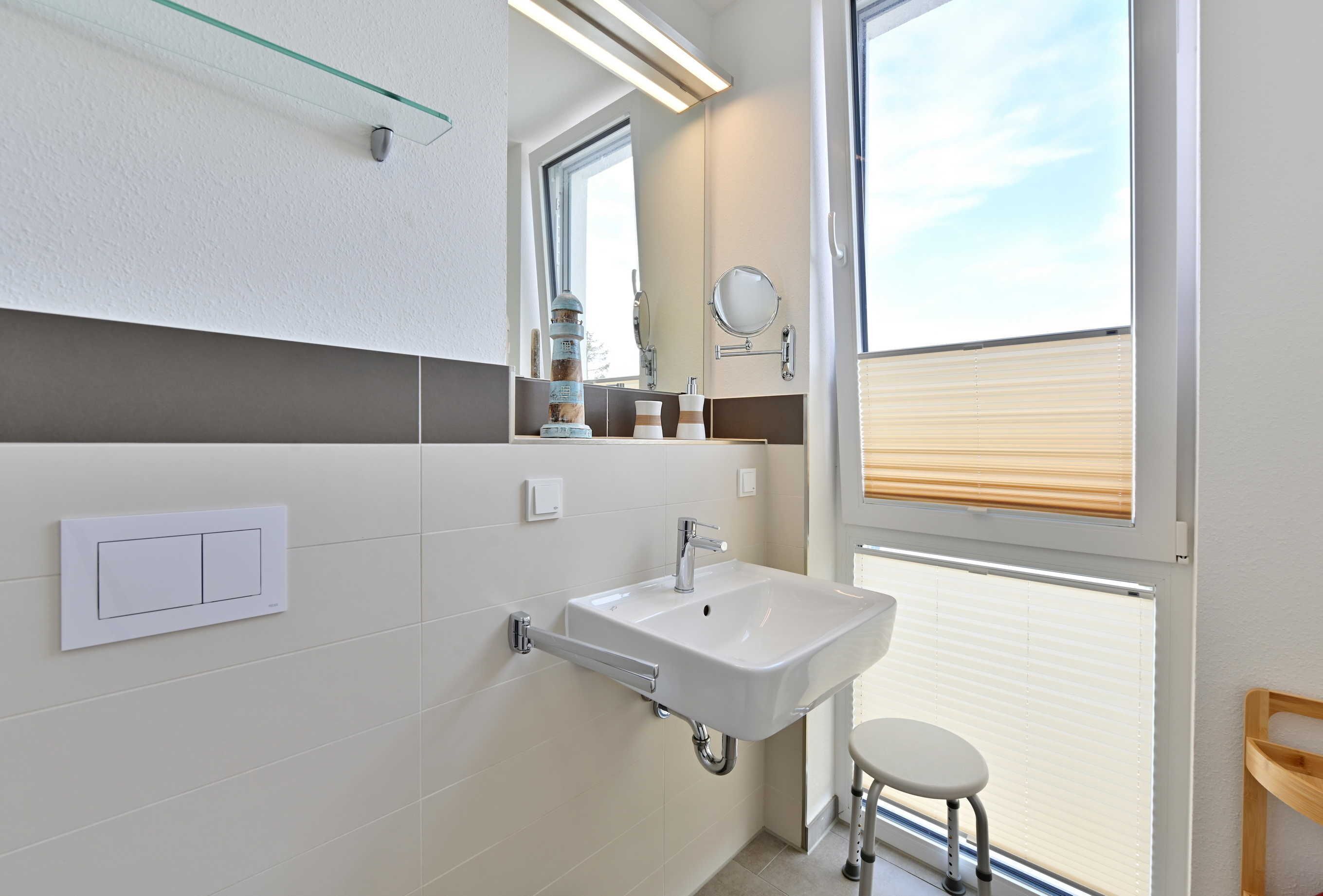 Une salle de bain moderne avec un lavabo blanc, un miroir et un petit tabouret.