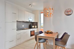 Une cuisine moderne avec des armoires blanches, un four encastré et un coin repas comprenant une table en bois et deux chaises.