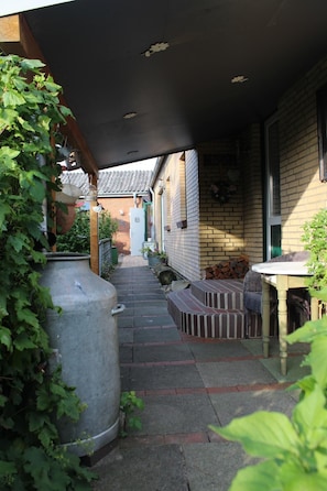 Een overdekt buitengebied met een bakstenen muur, een grote plantenbak en een tafel met stoelen.