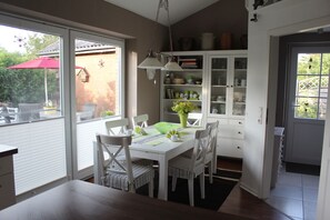 Een eetgedeelte met een witte tafel en stoelen, een vaas met bloemen en een kast met glazen deuren.