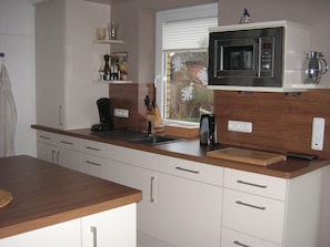 Een moderne keuken met witte kasten, een houten aanrecht, een ingebouwde magnetron en een raam met uitzicht.