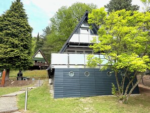 A modern building with a sloped roof, surrounded by trees and a wooden structure in the background.