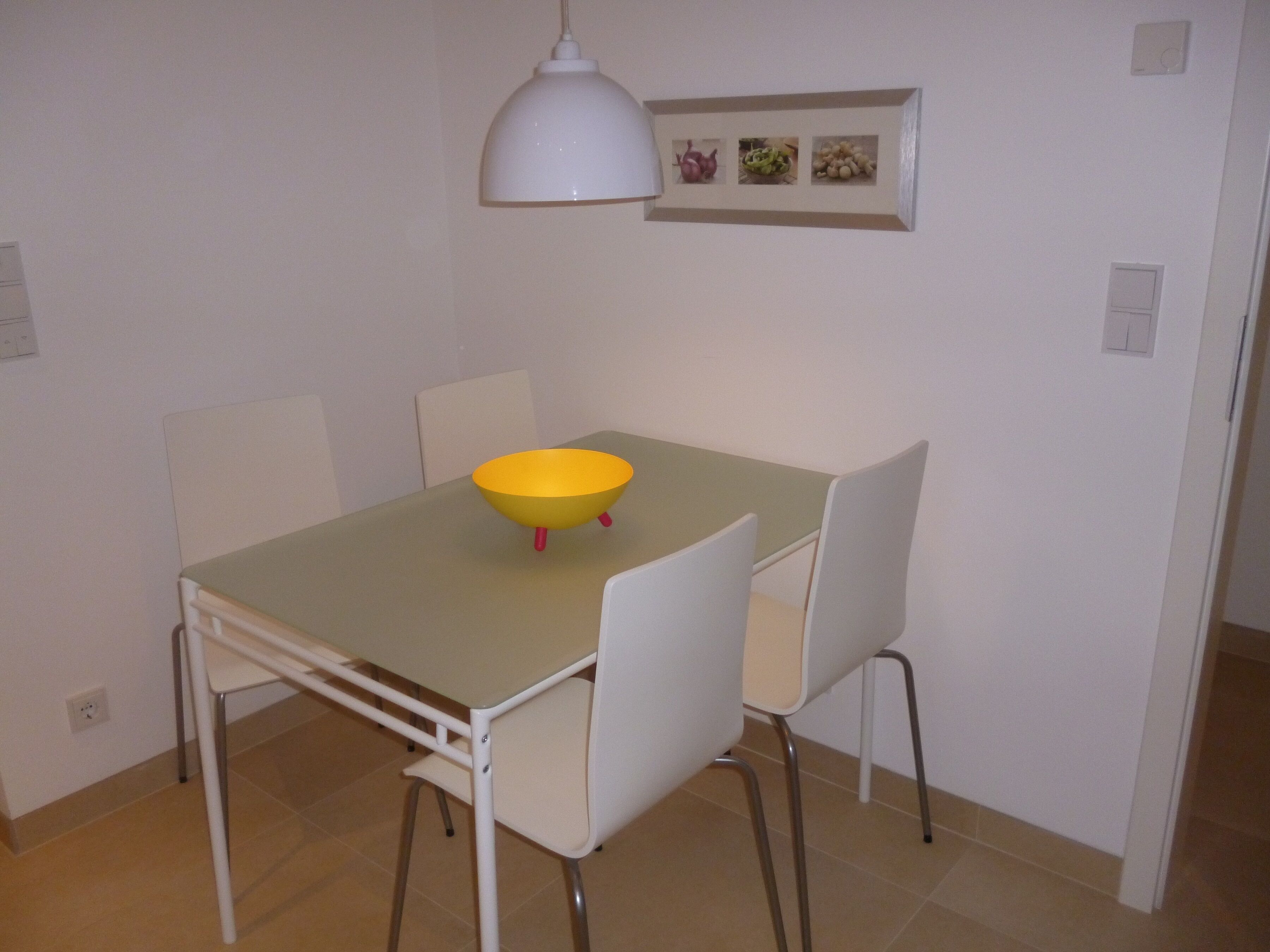 A dining area with a table, chairs, a bowl, a pendant light, and a wall-mounted picture frame.