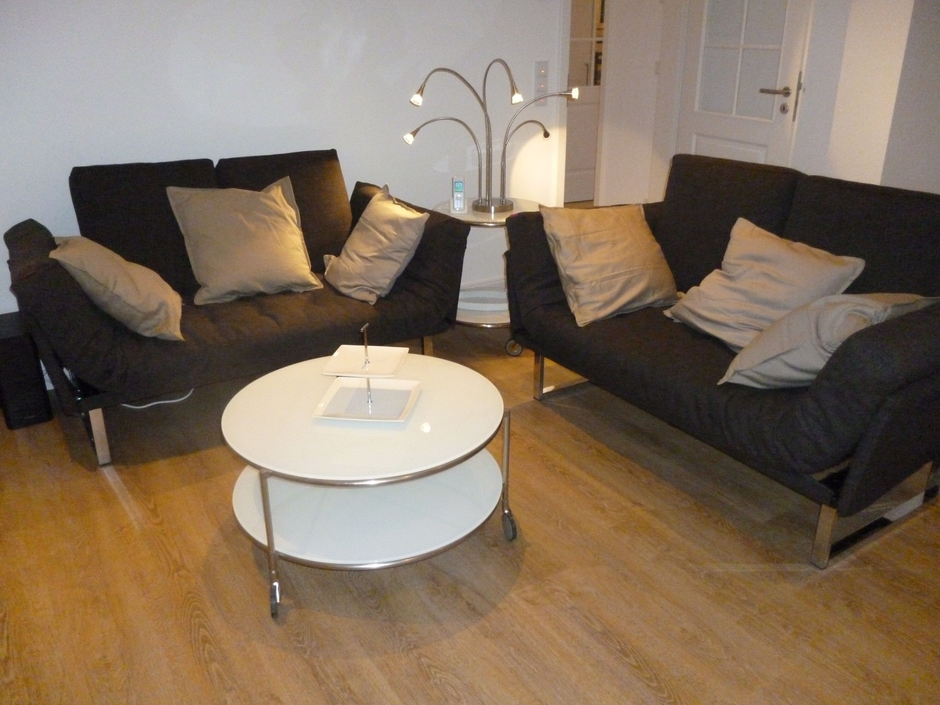 Ein modernes Wohnzimmer mit zwei dunklen Sofas, einem weißen Couchtisch und einer Stehlampe.