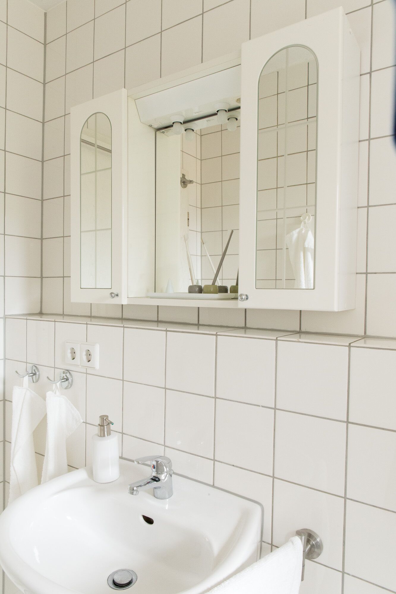 A bathroom with white tiled walls, a sink with a mirror above it, and two towels hanging on hooks.