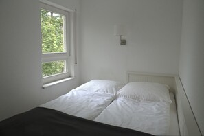 A simple, clean room with a bed, a window, and a wall-mounted light fixture. - Dresden Strehlen - Charming apartment for two to four people (Dresden)