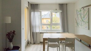 Ein Essbereich mit Tisch und Stühlen, ein Fenster mit Vorhängen sowie eine Wand mit abstrakter Kunst.