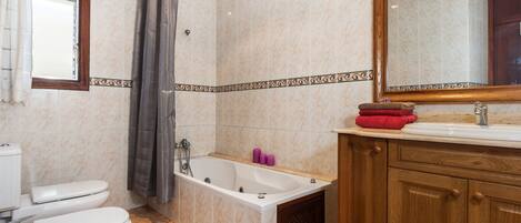 A bathroom with a toilet, bathtub, and wooden vanity with a mirror.