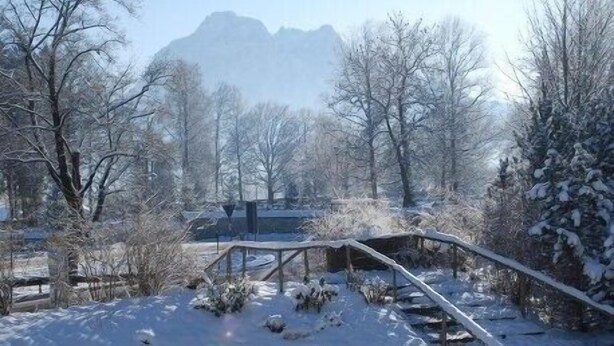 Un paysage enneigé avec un pont en bois, des arbres et une montagne en arrière-plan.