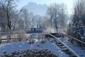 A snow-covered landscape with a wooden bridge, trees, and a mountain in the background.