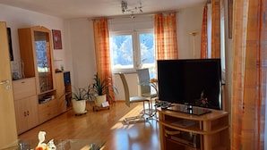 Un salon avec un téléviseur posé sur un meuble en bois, un buffet en bois, une chaise et une plante en pot.