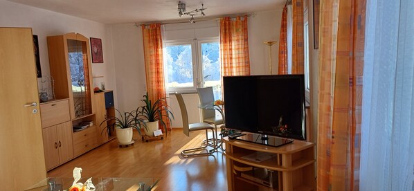 A living room with a TV on a wooden stand, a wooden cabinet, a chair, and a potted plant.
