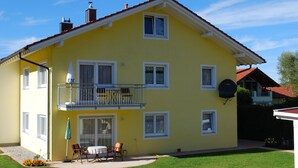 Un immeuble jaune à deux étages, doté d’un balcon, d’une antenne parabolique et d’une petite terrasse avec du mobilier d’extérieur.