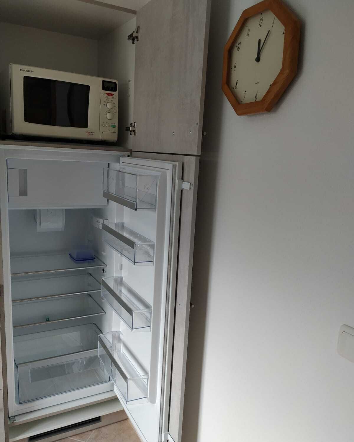 Une cuisine avec un four à micro-ondes posé sur le plan de travail, un réfrigérateur dont la porte est ouverte et une horloge accrochée au mur.
