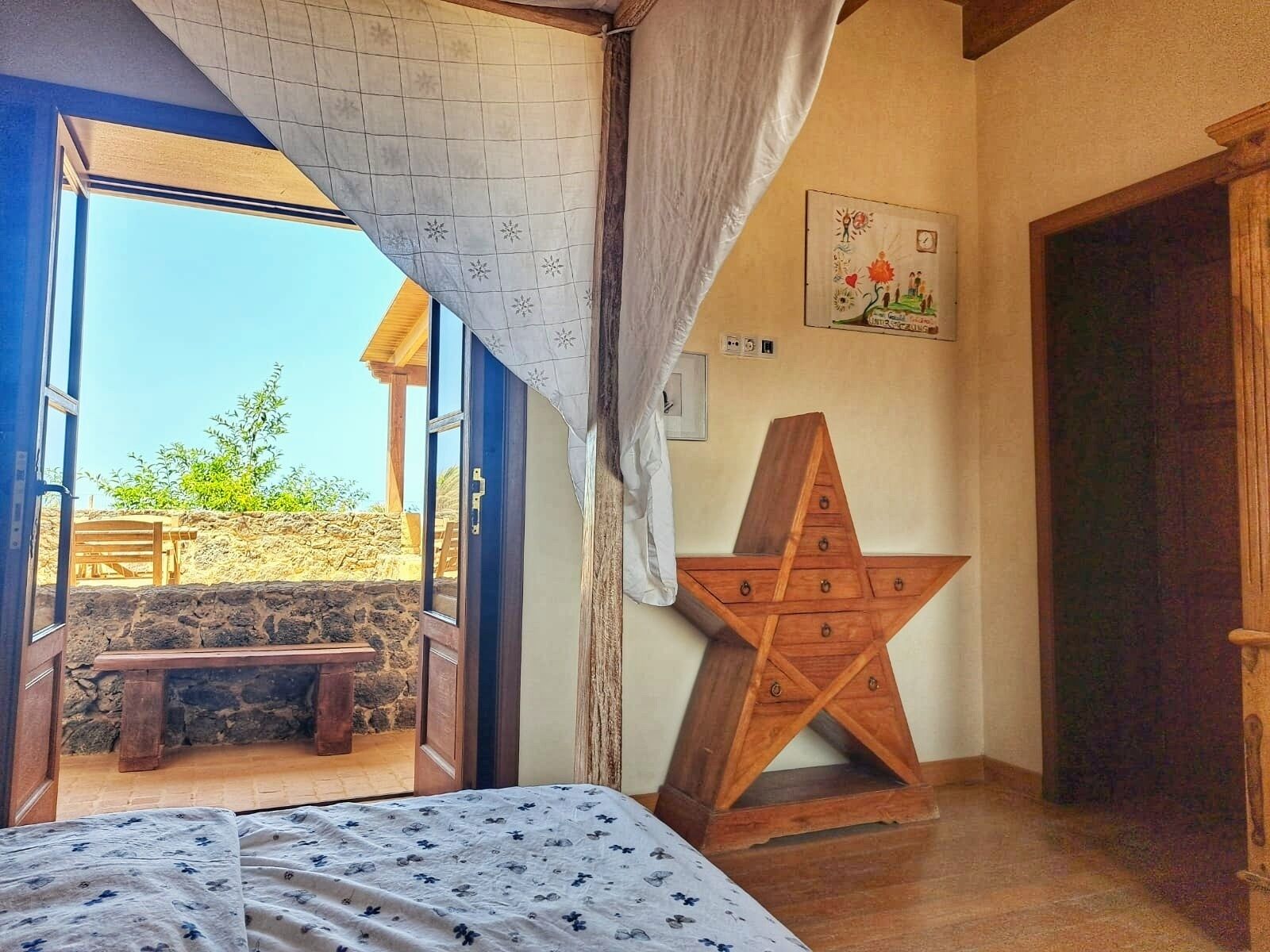 A bedroom with an open door leading to a patio, a wooden star-shaped nightstand, and a bed with a floral bedspread.