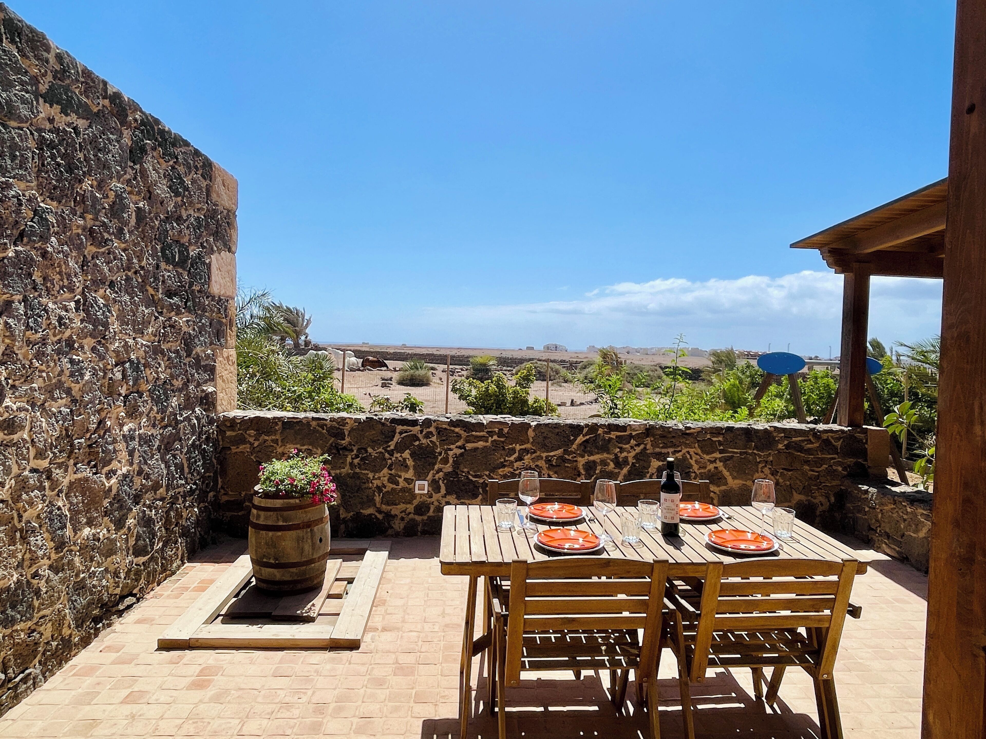 A stone wall, a wooden table with orange plates, and a view of a distant landscape.