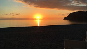 Un coucher de soleil sur une mer calme, avec la silhouette d'une falaise à l'horizon.