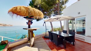 Une terrasse avec une table et des chaises, un parasol en chaume et une vue sur la mer.